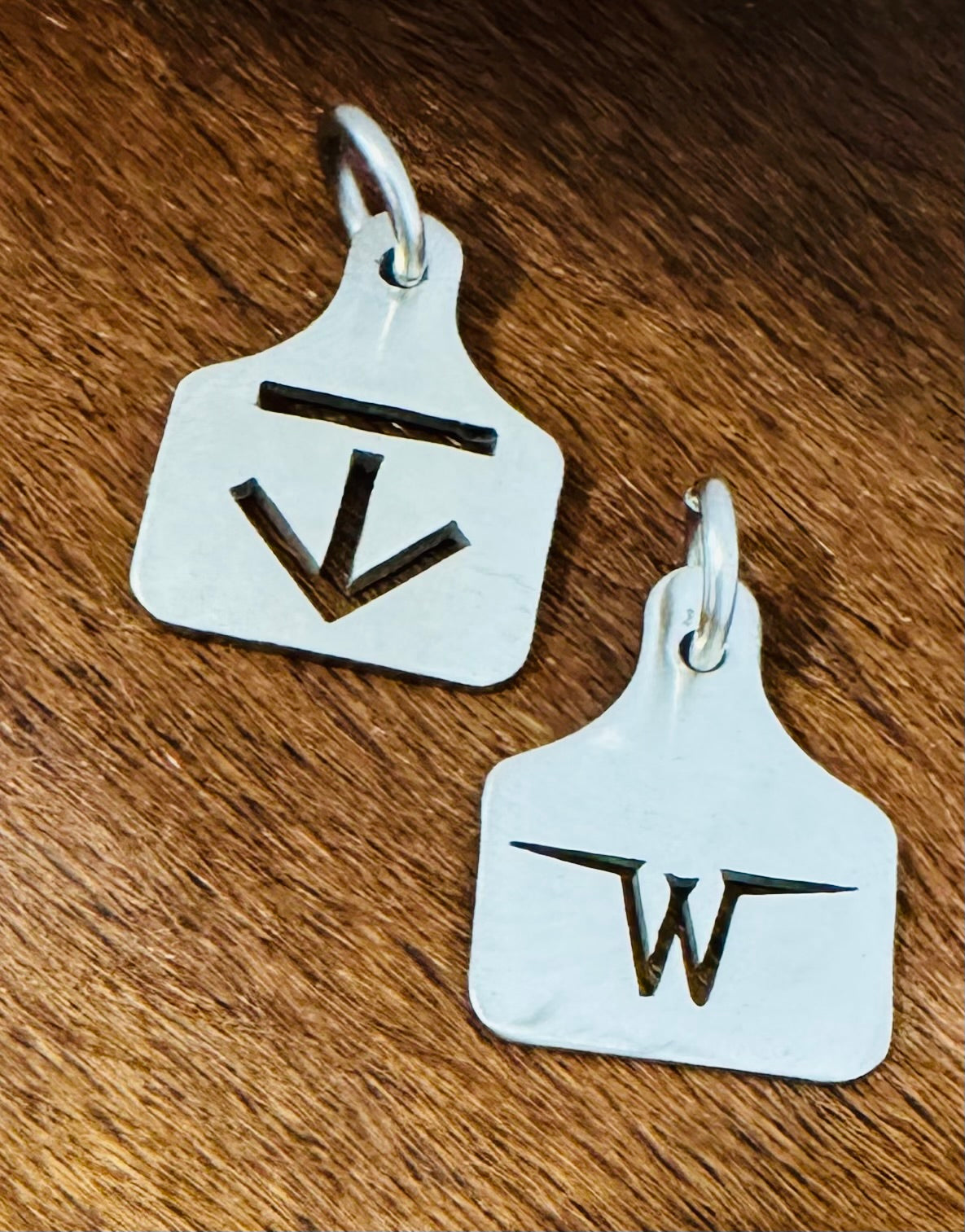 Two sterling silver ear tag pendants with an arrow brand and a W brand, on wood