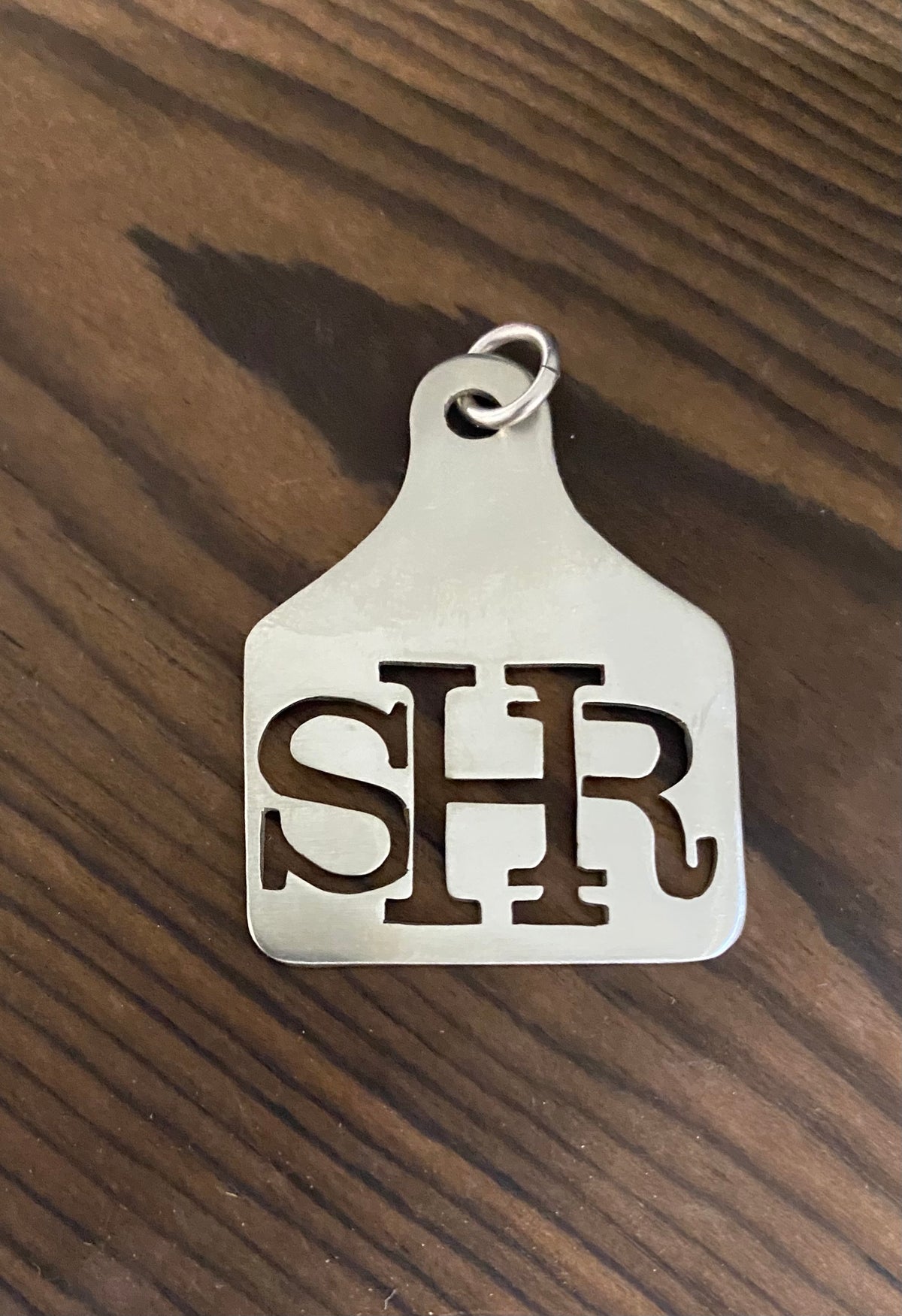 Sterling silver ear tag pendant with a connected SHR ranch brand, on dark wood
